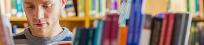banner: a close shot of a man who reads a book between book shelves in a library