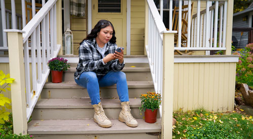 A Veteran accessing care on her cellphone while sitting on her front steps.