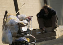 Photo of a homeless man sitting behind a shopping cart full of his possessions.