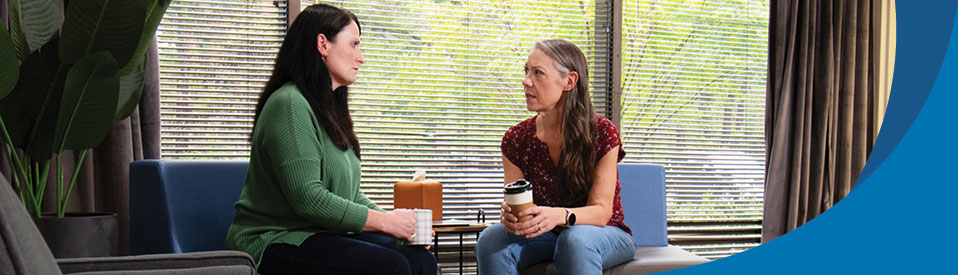 two female veterans sitting inside, drinking coffee, talking