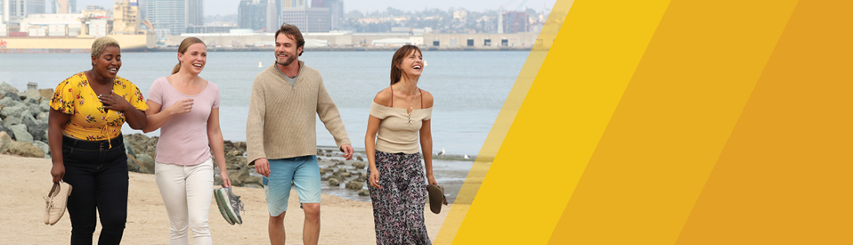 women and man walking on beach laughing